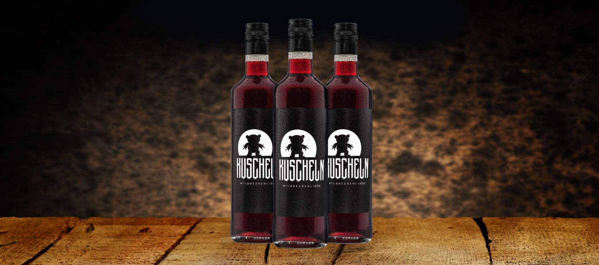 Drei Flaschen KUSCHELN Likör stehen auf rustikalem Holztisch vor dunklem Hintergrund.